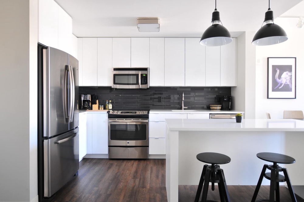 Moderne, weiße Küche mit Edelstahlofen, Mikrowelle, Kühlschrank und dunklem Holzboden.