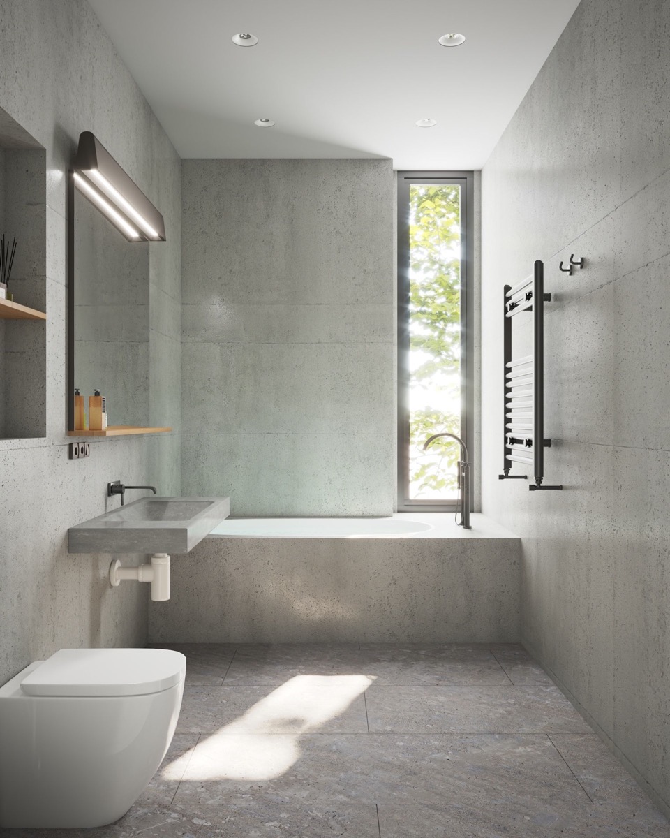 Modernes Badezimmer mit grauen Betonwänden und -boden, schmalem Fenster, weißer Toilette, grauem Waschbecken und beheiztem Handtuchhalter.