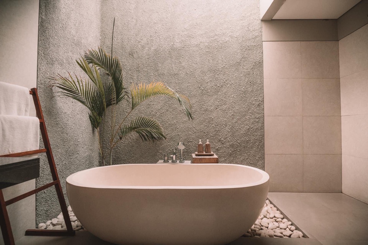Ein modernes Badezimmer mit einer ovalen Badewanne, einem Pflanzenblatt und einem Handtuchhalter.